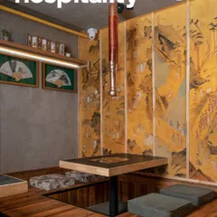 A closer view of the sunken dining nook at Seoul. The design combines warm wood flooring, concrete-finish walls, and curated cultural artifacts like framed fans to create a space that feels both modern and deeply rooted in heritage.