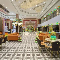 A full view of a jungle-themed party in a large banquet hall. The decoration includes a stage setup, marquee letters, and balloon arrangements placed around the room.