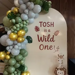 The 'Wild One' jungle theme is a huge hit for first birthdays. Here, I used an organic balloon arch in sage green, white, and gold around a custom arched panel, complete with cute jungle animal cutouts.
