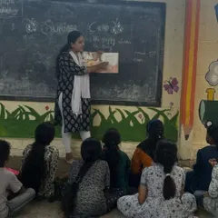 A storytelling session in progress at the Makkala Masti summer camp. A volunteer reads a picture book to an attentive group of children, fostering a love for reading and language.