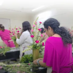 A student carefully adds pink carnations to her vertical arrangement. This photo captures the concentration and hands-on nature of our classes, where you learn by doing.