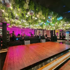 We create the perfect party atmosphere with elements like this expansive wooden dance floor set under a ceiling of hanging greenery and disco balls. The pink and purple lighting sets the mood for a night of dancing.