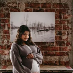A quiet, reflective moment for this beautiful mom-to-be. The makeup is minimal and soft, with a focus on a healthy, glowing complexion against a rustic brick backdrop.