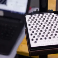 A close-up of a case of air rifle pellets, the essential component for precision shooting, with a laptop for data analysis in the background.