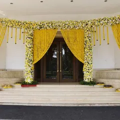 A grand entrance decorated with traditional marigolds. The wide archway is covered in yellow and white flowers with hanging marigold strings, creating a classic and auspicious welcome for a day wedding.