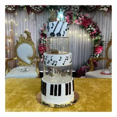 A magnificent 5-tier spacer cake with a music theme for a 60th birthday. This blueberry-flavored cake features piano keys, musical notes, and a guitar topper, all brought together with fairy lights in the spacers.