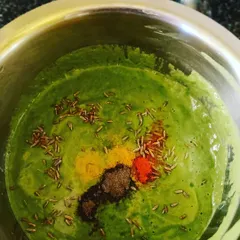 Preparing the batter for a healthy besan palak chilla, with spices like cumin, turmeric, and chili powder being added.