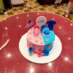 A classic 'She or He' gender reveal cake, perfectly decorated with pink and blue shoes, a dress, and a t-shirt. It’s a sweet centerpiece for the celebration.