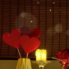 Simple romantic details for a Valentine's or anniversary setup. An LED candle provides safe, warm light next to a small bouquet of red heart props, adding a sweet and thematic touch.