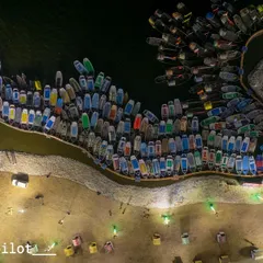 A top-down drone view of the boats, or 'naav', clustered at Sangam. This unique angle reveals a colorful mosaic against the dark water, a perspective you can only get from the sky. It shows the scale and life of our ghats.