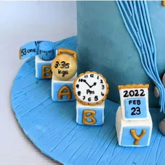 A closer look at the custom birth announcement toppers. Each block features a hand-painted detail, like the calendar, clock, and kettlebell, making it a unique and memorable part of a baby welcome cake.