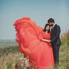 A tender moment on a grassy hill, with the bride's vibrant red gown billowing in the wind. This shot combines natural beauty with the drama of a flowing dress for a stunning pre-wedding portrait.