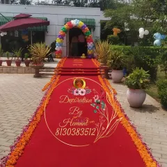 A grand entrance for a baby boy's welcome party. A long red carpet, lined with marigold flowers, leads to a colorful rainbow balloon arch at the doorway, creating a spectacular welcome.