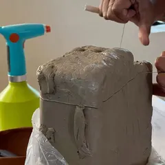 Preparing a block of clay by cutting it with a wire tool. This process, known as wedging, removes air bubbles and ensures the clay has a consistent texture, making it ready for sculpting or throwing.