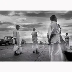 Men stand on a pier on Agatti Island, Lakshadweep, looking out towards the sea under a dramatic sky. This black and white documentary photograph from 1998 captures a sense of waiting and contemplation, a timeless slice of island life.