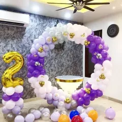 A circular balloon frame decorated with purple, white, and gold balloons. A large gold foil number '2' marks the milestone.