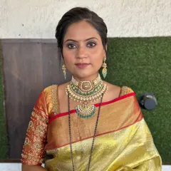 An elegant and regal look for a bride in a traditional gold saree. The makeup is kept classic with a defined eye, and the look is completed with beautiful green-toned jewelry.