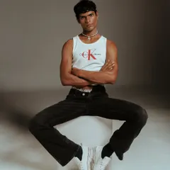 A full-length seated pose that showcases the complete Calvin Klein look, from the tank and jeans to the classic white sneakers. This composition is designed to feel both relaxed and powerful, a key theme in my menswear direction.