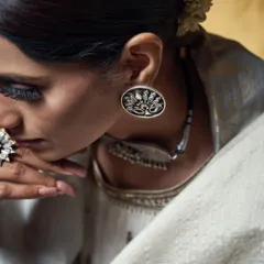 A detailed shot focusing on handcrafted ethnic jewelry. The lighting is carefully controlled to accentuate the craftsmanship of the silver earring and the model's contemplative expression.