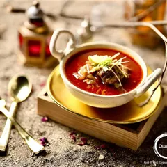 The complete Mutton Nalli Nihari experience, presented in a traditional bowl with elegant cutlery. The rustic, sandy backdrop highlights the dish's authentic and royal origins.