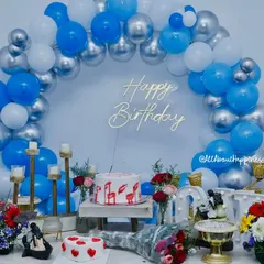 The decor without the special lighting, showing the beautiful blue and silver balloon arch and the detailed table setup with cakes and flowers.