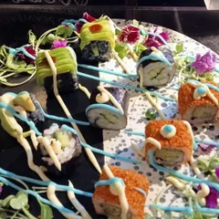 An example of our creative sushi plating. Here, assorted sushi rolls are arranged on a dark platter and garnished with colorful sauces and edible flowers, turning a classic dish into a modern culinary creation.