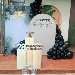 For a more modern and stylish celebration, I offer elegant setups like this 'Chapter 28' birthday. It features a sophisticated black and marble-effect backdrop, a custom arched sign, black chrome balloons, and sleek pedestals for the cake.