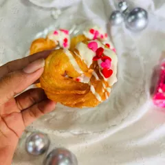 Here is a close-up of my signature heart-shaped churro. You can see the crispy, golden texture of the churro, generously drizzled with creamy white chocolate and topped with red and pink heart-shaped sprinkles for a festive touch.