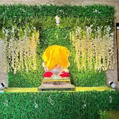 I can create a lush, natural-looking backdrop for your Ganpati idol. This decoration features a dense green wall with cascading white wisteria flowers, bringing a touch of nature indoors for the festival.
