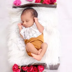 This full-body shot displays a beautiful outfit with a lace collar, set against a plush white fur rug. The addition of fresh pink roses adds a gentle pop of color to this classic newborn setup.