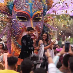 Chasing thrills and making memories. A couple makes a grand entrance at their carnival-themed party on a massive, ornate float with a Venetian mask.
