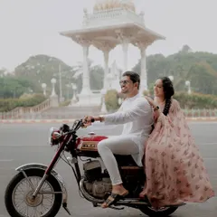 A couple enjoys a ride on a classic Yezdi motorcycle through the streets of Mysore, blending vintage charm with the city's royal heritage. This shows how we can create a unique, themed pre-wedding shoot.