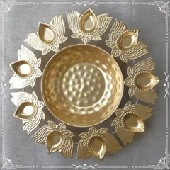 A stunning golden urli platter with an outer ring of lotus-shaped diyas. This piece is a perfect centerpiece for Diwali or any pooja, designed to be filled with water, flowers, or festive treats.