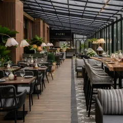 The al fresco dining area at FIORI, Lonavala, where the design seamlessly merges with the surrounding nature. A retractable glass roof and full-height windows allow for an immersive experience, complemented by a natural material palette of stone and wood-finished aluminum.