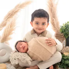 A proud big brother holds his newborn sibling in this boho-themed newborn shoot. The natural textures and warm tones create a dreamy, gentle setting for this beautiful moment.