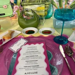 A close-up of a place setting from a couture brunch, showing a personalized menu and artfully smeared sauces that mimic a painter's palette. Every detail is designed to align with the event's creative and high-fashion theme.
