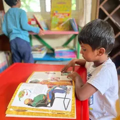 A young boy sits at a child sized table, carefully studying the illustrations in a large book. Our space is equipped with furniture that is perfect for little learners.