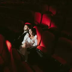 A moody and dramatic portrait of the couple in the theatre. The spotlight creates a strong contrast, highlighting them amidst the rows of empty red seats and creating an atmosphere of intimacy and focus.