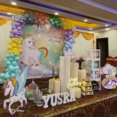 This magical Unicorn theme is perfect for a 3rd birthday and ear-piercing ceremony. It includes a pastel rainbow balloon arch over a large unicorn backdrop, character cutouts, 'BABY' blocks, and a neon 'Happy Birthday' sign.