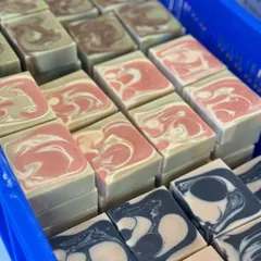 A crate full of our diverse cold process soaps, including the green Superfood bar, the pink and green Plumeria bar, and the black and white Mint Charcoal bar.