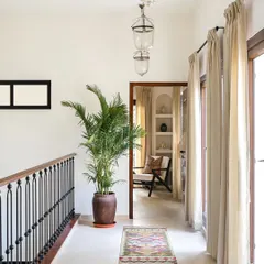 Even in-between spaces like hallways deserve attention. On the first floor of the Modern Spanish Home, the custom black iron railing continues, complemented by a colorful runner rug and a large potted palm that adds life and vertical interest.