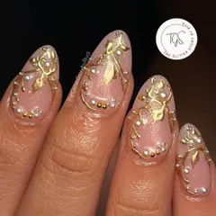 A detailed close-up of 3D nail art for a bride. This design uses sculpted gold vines and individually placed pearls on a sheer pink base to create a delicate, luxurious look.