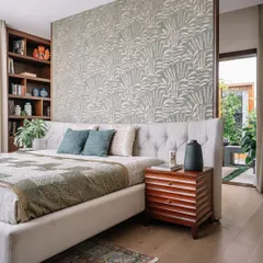 This bedroom combines comfort with clever design. A beautiful floral wallpaper creates a feature wall that doubles as a partition, with a built-in bookshelf behind the bed for storage. The tufted wingback bed adds a touch of classic elegance.