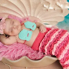 A magical 'Baby Mermaid' theme. This newborn is dressed in a crocheted mermaid tail, sleeping peacefully in a giant seashell prop against a serene ocean backdrop for a truly enchanting portrait.