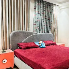 A simple and sweet kid's bedroom with a comfortable bed, playful printed curtains, and a pop of color from the orange bedside table.