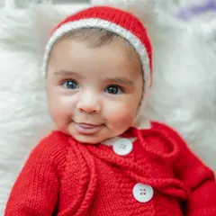 A close-up of a newborn's sweet face during a Christmas shoot. The soft, knitted Santa outfit keeps the baby cozy and adds to the festive charm.
