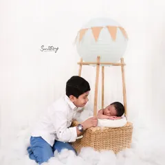 Including siblings in themed shots can be so much fun. Here, a proud big brother looks on as his new baby sister rests in the hot air balloon basket, creating a sweet story of shared adventure.