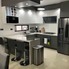 This U-shaped kitchen layout maximizes counter space and storage. It features high-gloss white cabinets for a clean look, contrasted with dark grey lower cabinets. The design includes a breakfast bar for casual dining and integrated appliances for a seamless finish.