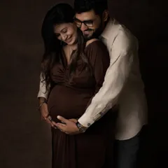 A tender embrace against a dark, classic backdrop. The focus is entirely on the couple's connection and the baby they are waiting for.