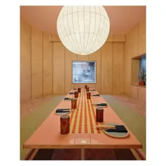 A private dining room at Lucky Chan, featuring a long table with a custom tile runner. The space is enclosed with wood paneling and illuminated by a large, handmade raw silk lamp, creating a warm and intimate setting.